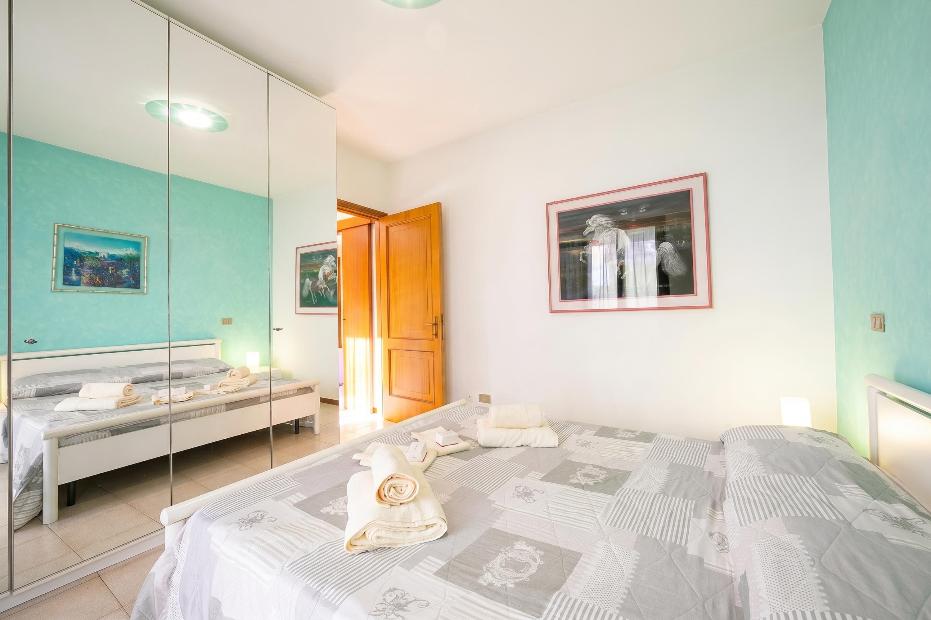 Een slaapkamer met een bed, een spiegel, een kledingkast en een schilderij aan de muur.