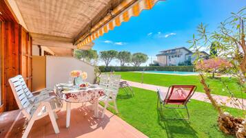 Une terrasse couverte avec une table dressée pour les repas, des chaises d’extérieur et une vue sur une piscine et une maison en arrière-plan.