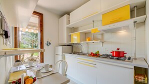 A modern kitchen with white cabinets, a yellow accent, a gas stove, and a dining area with a table set for breakfast. - Cinzia Apartment Front Beach- Pool, Garage & Terrace (Sirmione)