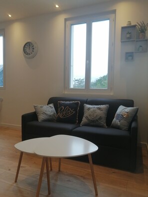 A living room with a black sofa, white table, and a large window. - Le Courlis, two minutes from the beach (Hauteville-sur-Mer)