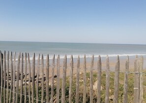 A wooden fence with barbed wire in front of a beach with calm waves and a clear sky. - Le Courlis, two minutes from the beach (Hauteville-sur-Mer)
