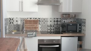 Cocina compacta con armarios blancos, microondas, horno integrado y un cubo de basura de acero inoxidable.