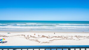 A beach with a clear blue sky, sandy shore, and a few people and umbrellas.