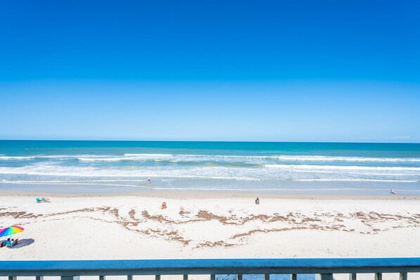 A beach with a clear blue sky, sandy shore, and a few people and umbrellas.