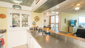 A kitchen with a stainless steel sink, a clock, and a dining area with a view of the ocean.
