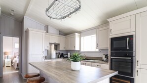 A modern kitchen with white cabinets, a wooden island with stools, a stainless steel range hood, a built-in oven, and a hanging light fixture.