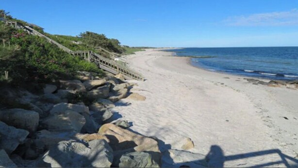 Ein Strand mit einer Holzpromenade und großen Felsen.