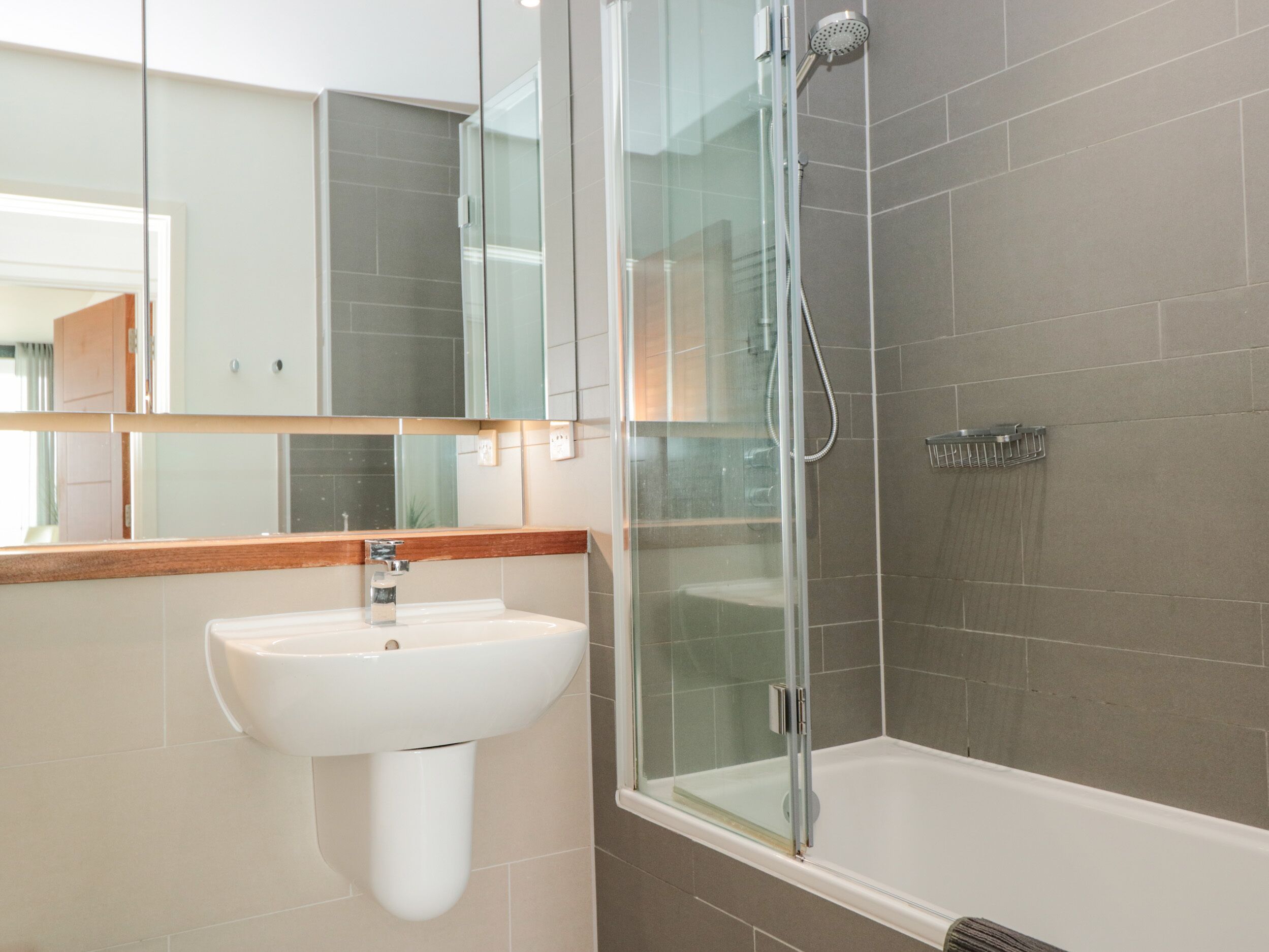 A modern bathroom with a glass-enclosed shower, a white sink, and a mirror above it.