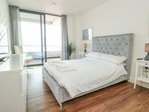 A modern bedroom with a large bed, a desk, and a view of the sea through a sliding glass door.