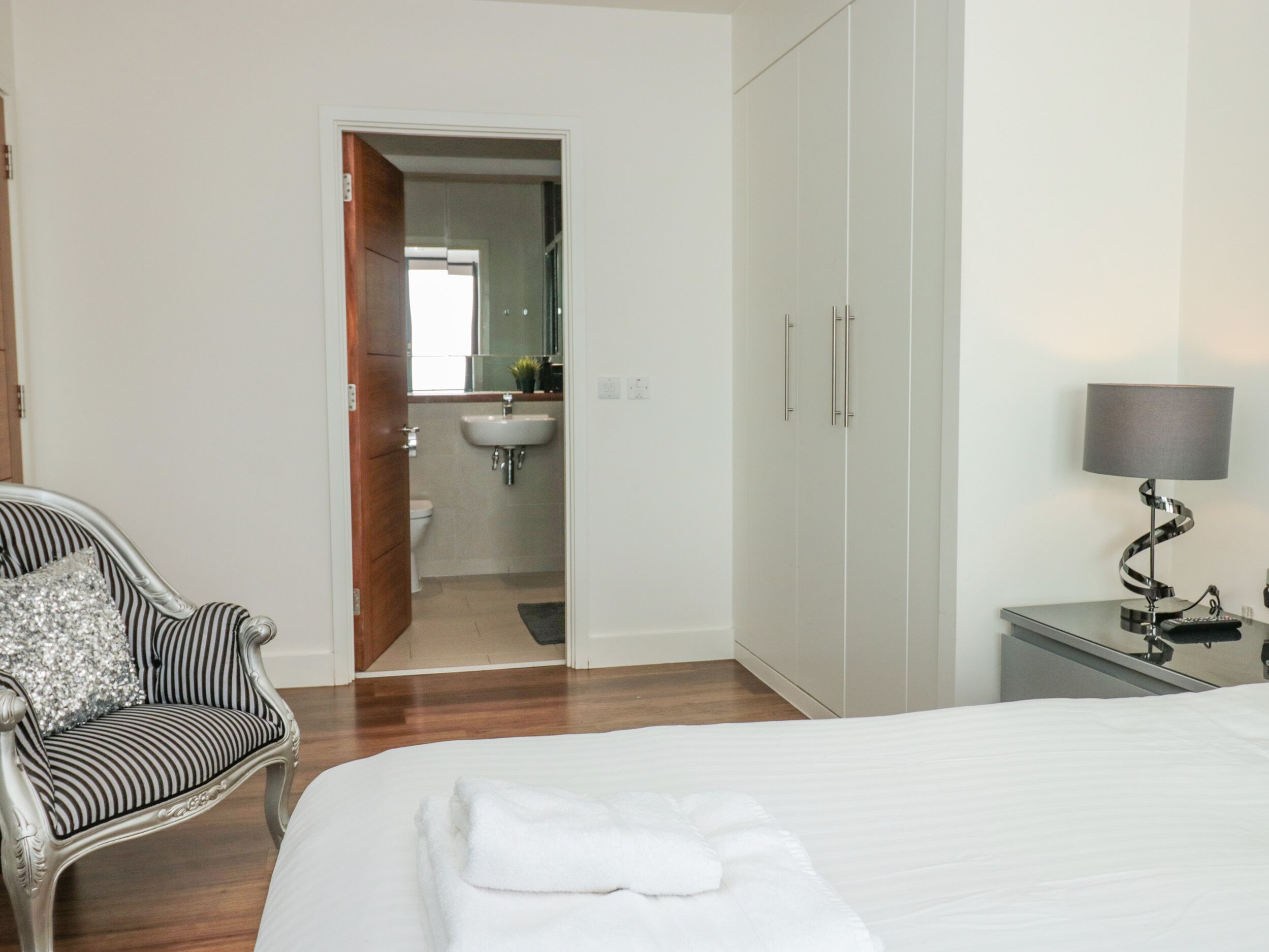 A bedroom with a bed, a bedside table with a lamp, a chair, and a wardrobe.