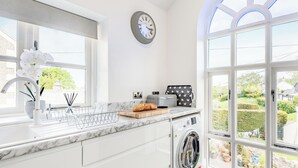 Una cocina moderna con lavadora integrada, un ventanal con vistas al jardín y un reloj en la pared.