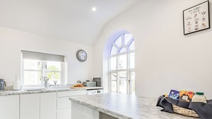 Una cocina moderna con armarios blancos, encimera de mármol y un amplio ventanal.