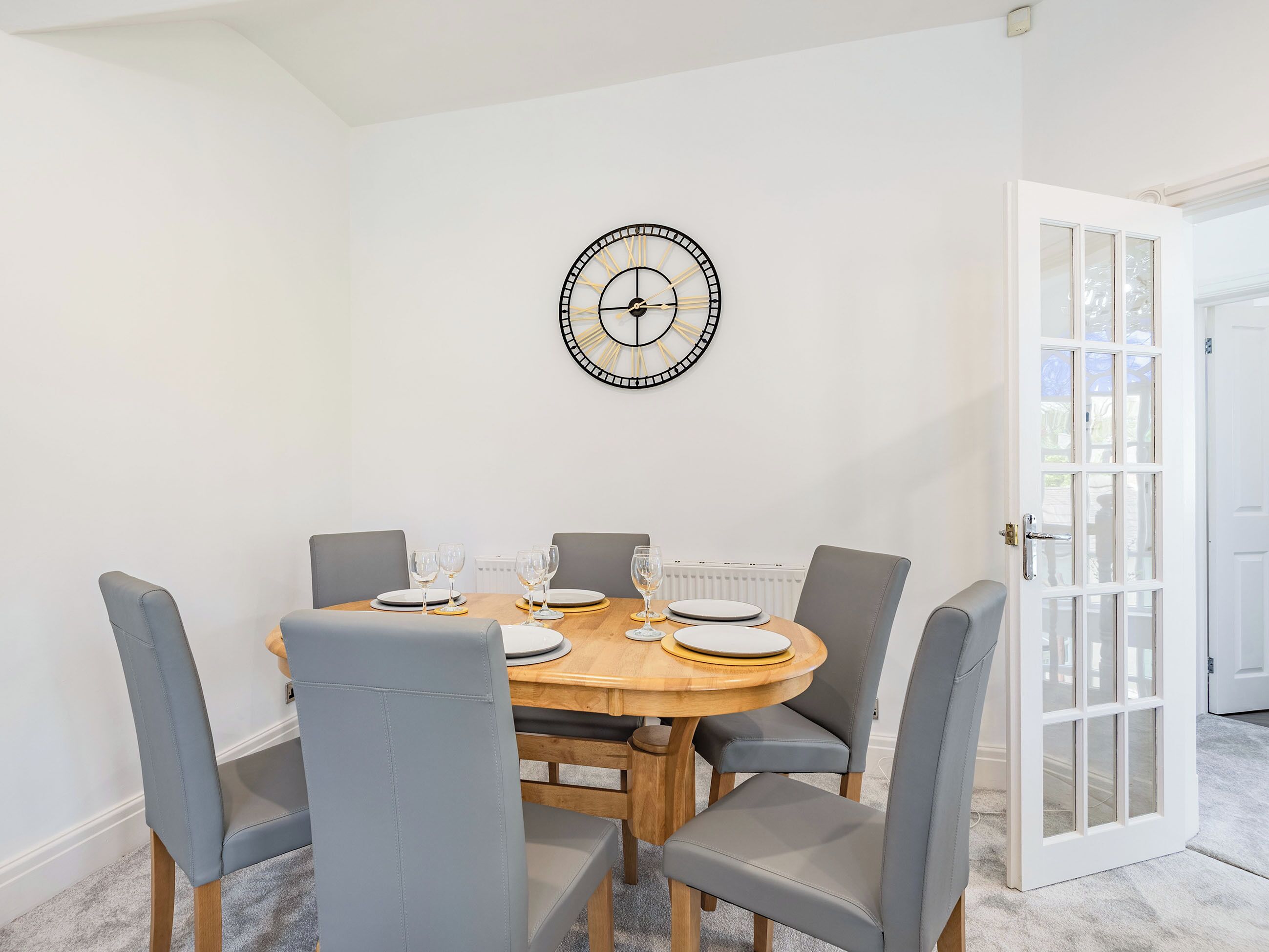 Un comedor con una mesa redonda de madera, sillas tapizadas de gris y un reloj fijado a la pared.