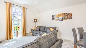Una sala moderna con un sofá gris, una lámpara de pie y un ventanal con cortinas.