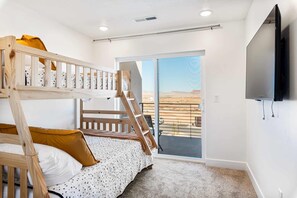 A bedroom with a bunk bed, a flat-screen TV, and a balcony with a view of the desert.