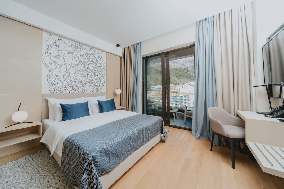 Ein modernes Hotelzimmer mit einem großen Bett, einem Schreibtisch und einem Balkon mit Vorhängen.