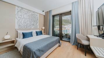 A modern hotel room with a large bed, a desk, and a view of a cityscape through the window.