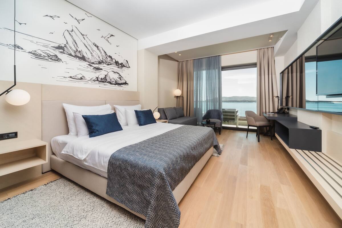 Ein modernes Hotelzimmer mit einem großen Bett, einem Schreibtisch und Blick auf das Meer.