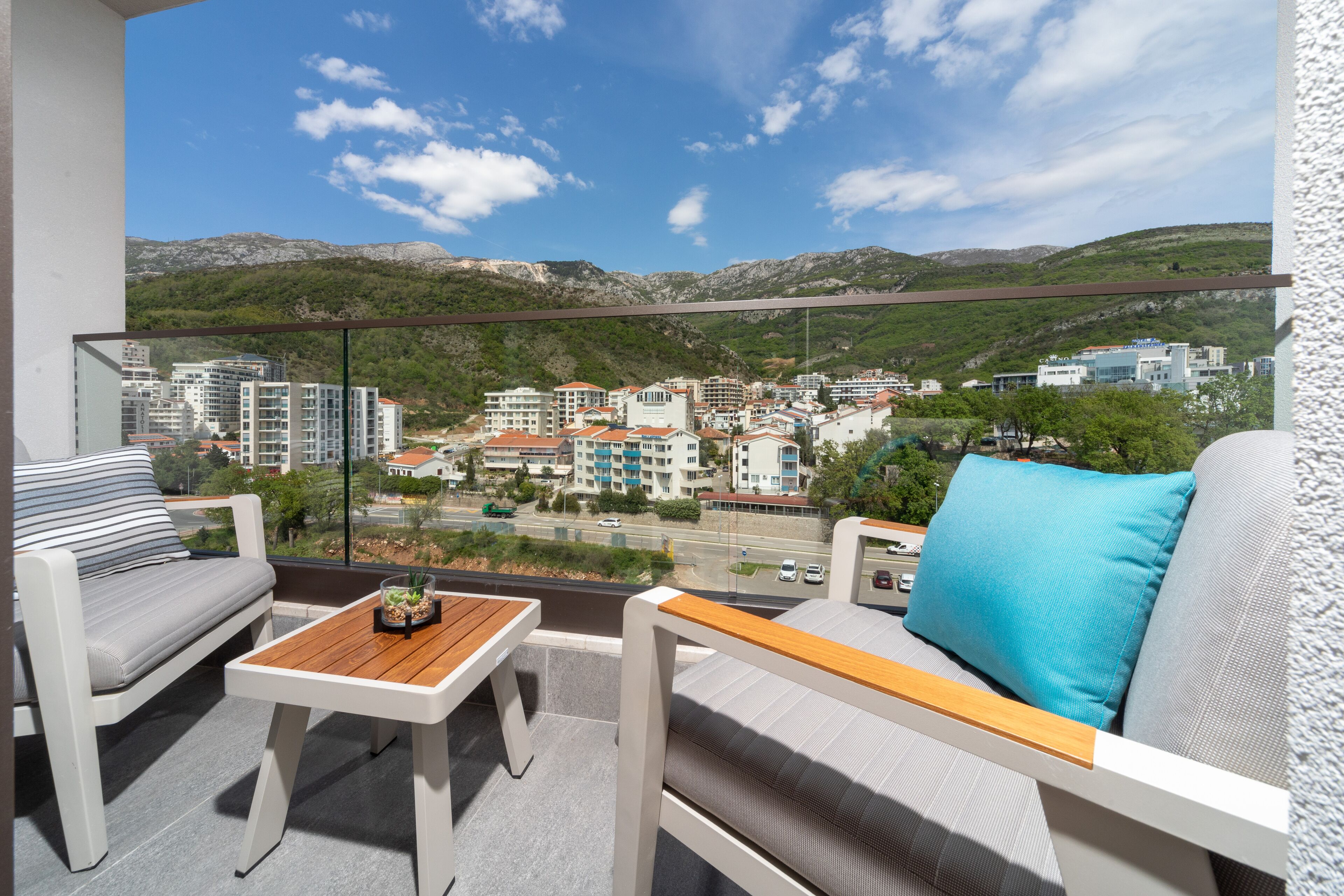 Ein Balkon mit einer Couch, einem kleinen Tisch und Blick auf eine Stadtlandschaft mit Gebäuden und Bergen.