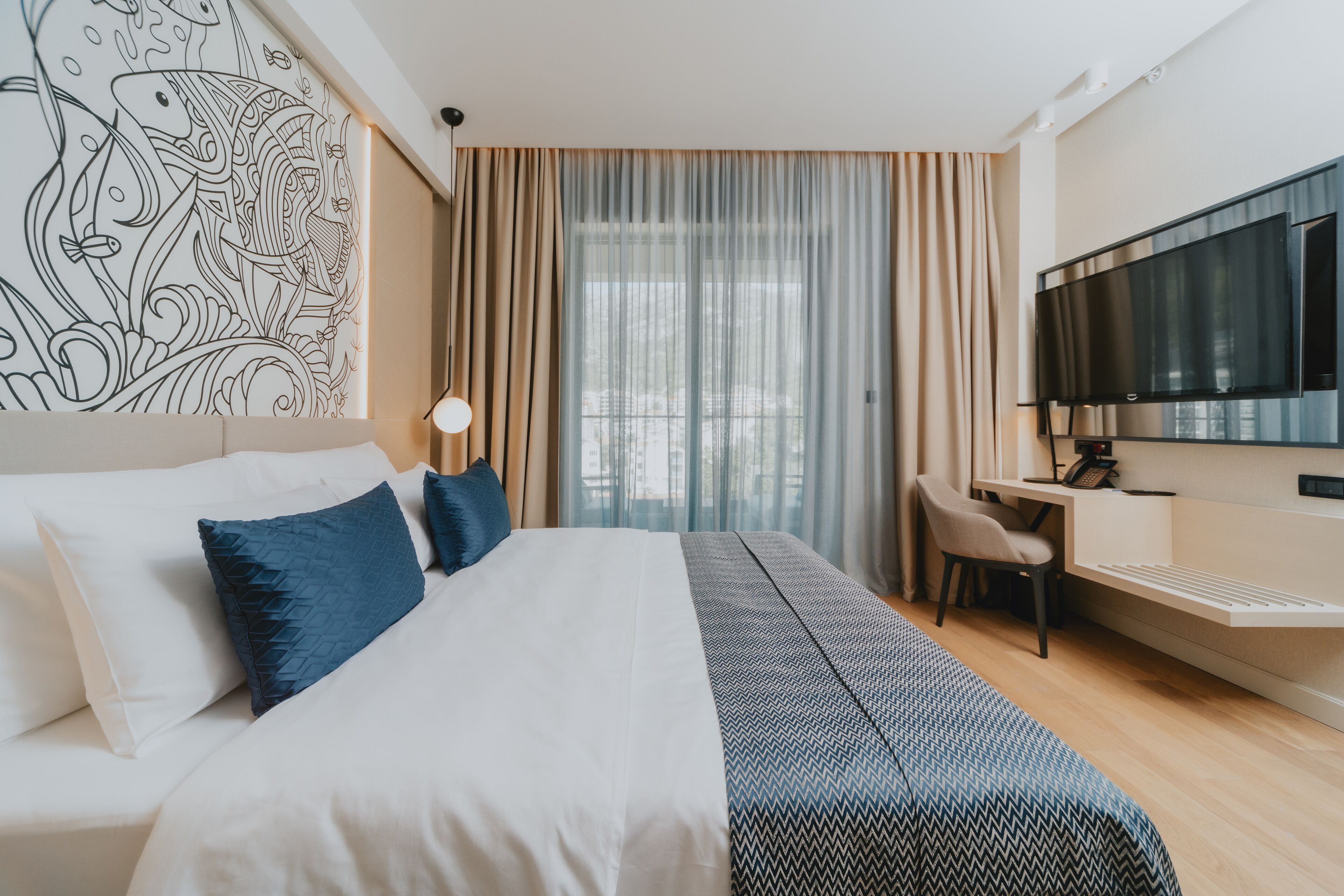 A hotel room with a bed, a desk, a chair, a TV, and a large window with curtains.