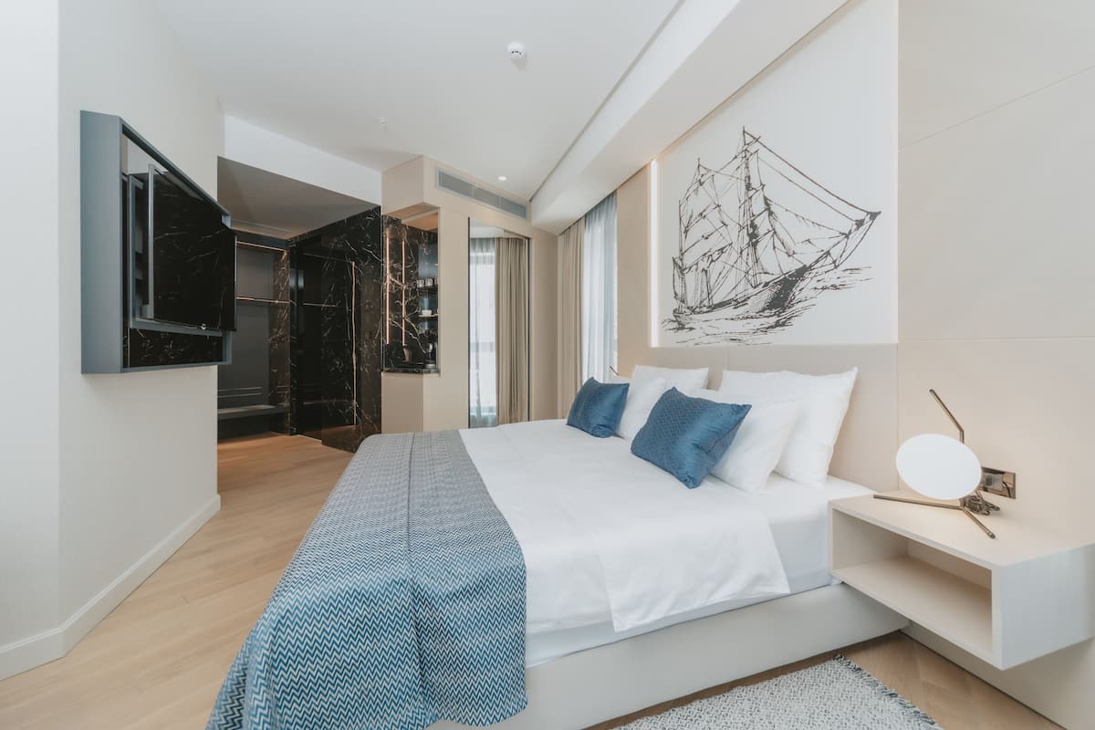 Ein modernes Schlafzimmer mit einem großen Bett, einem Flachbildfernseher, einem Gemälde und einem begehbaren Kleiderschrank.