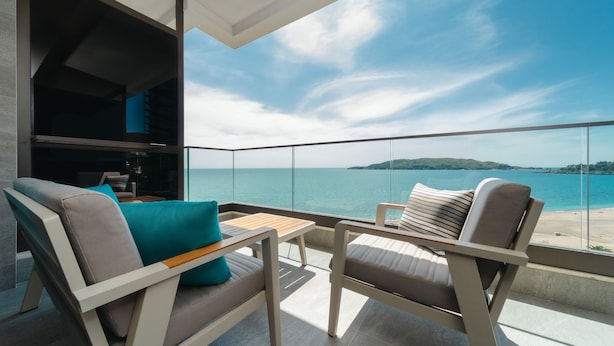 A balcony with a view of the sea, two chairs, a table, and a built-in seating area with cushions. - KATAMARE (Becici)