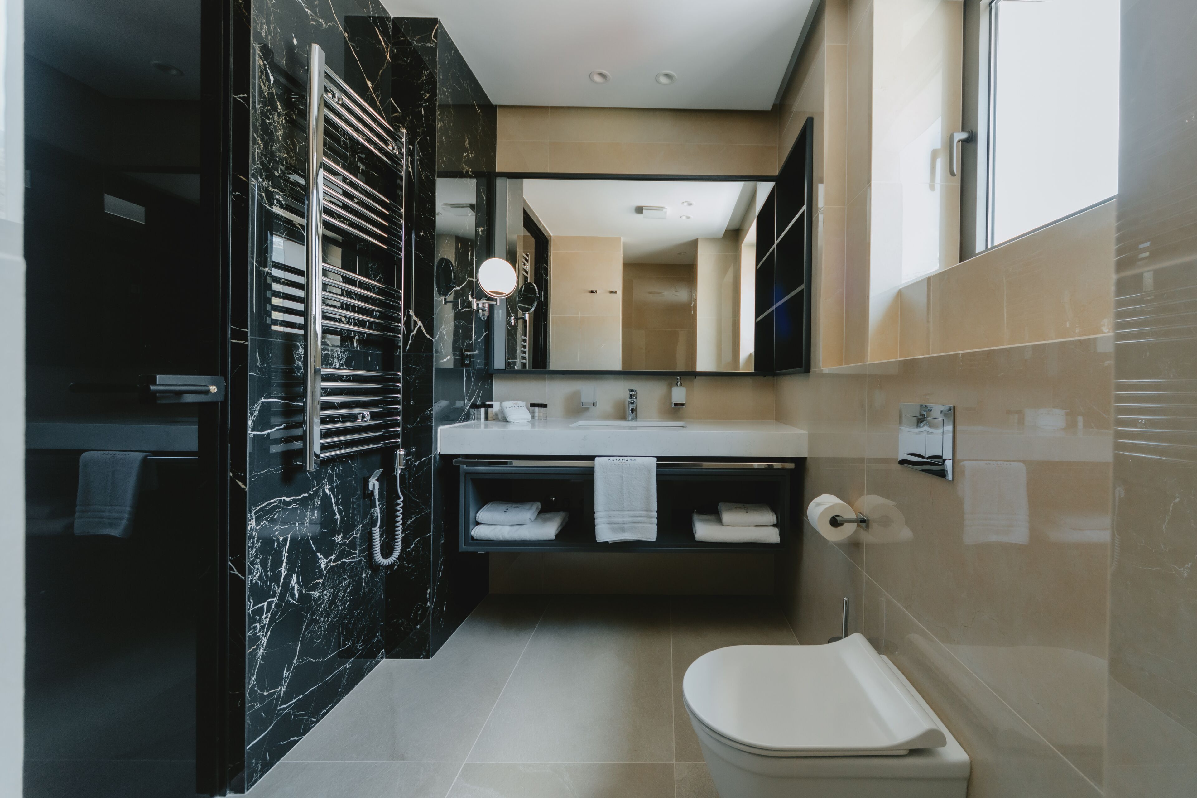 A modern bathroom with a marble vanity, a toilet, and a large mirror.