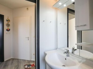 Une salle de bain moderne avec un lavabo blanc, un grand miroir et une porte agrémentée d’un tapis décoratif.