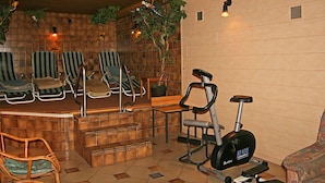 Un área de spa con cuatro sillones reclinables a rayas, un banco de madera, una mesita, una escalera y una bicicleta estática.