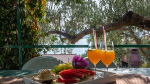 Ein Tisch mit einer Speisenplatte und zwei Gläsern Orangensaft, draußen mit Blick auf Bäume und ein Gebäude im Hintergrund.