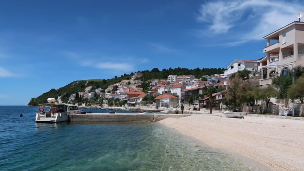 Eine Küstenstadt mit klarem Wasser, einem Sandstrand und Häusern mit roten Dächern.