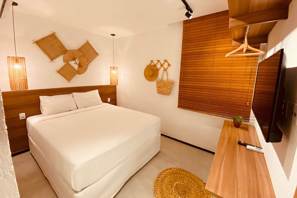 A bedroom with a large bed, wooden headboard, wall-mounted lamps, and a wooden desk with a plant.