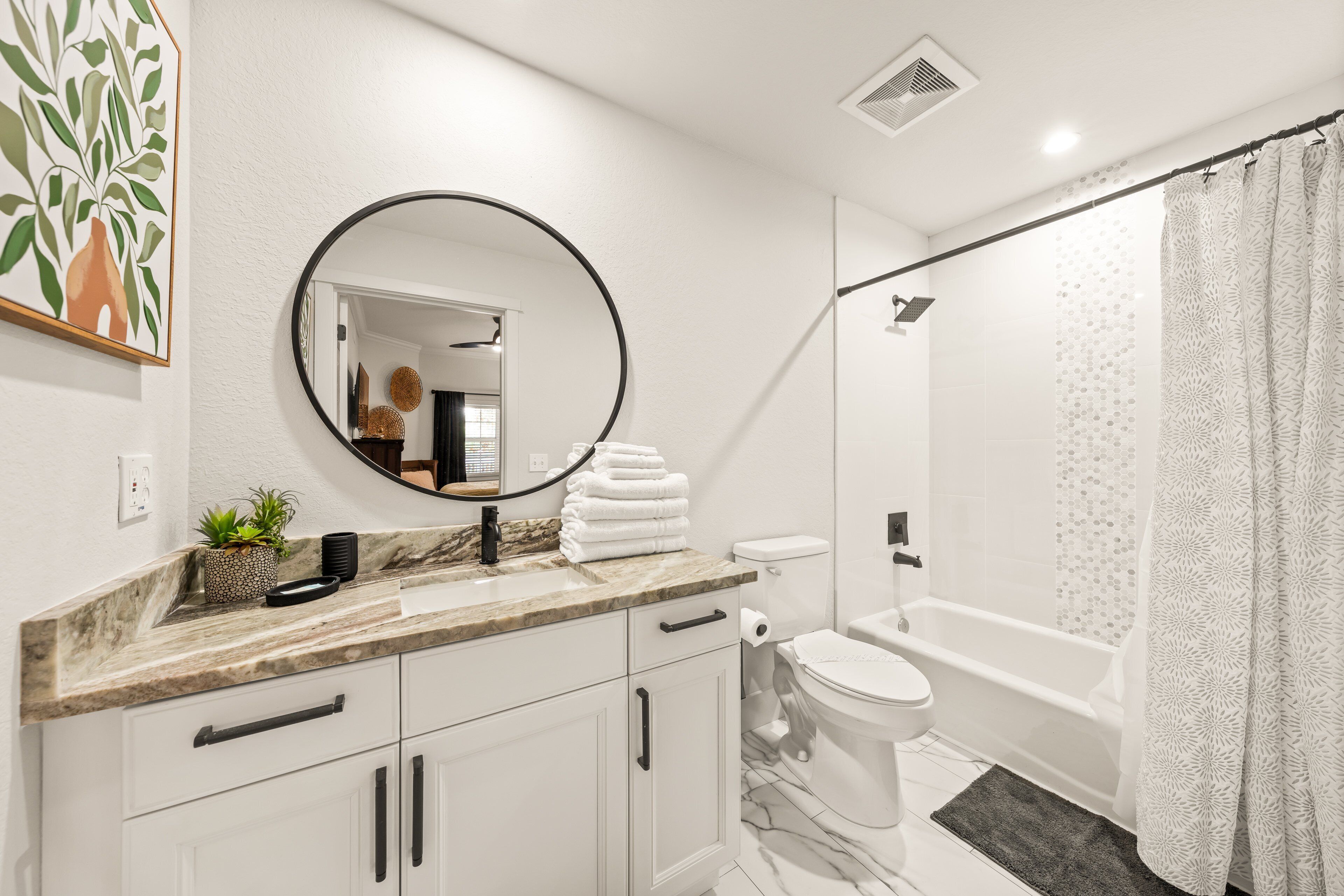 A modern bathroom with a marble countertop, a round mirror, a toilet, and a shower area.