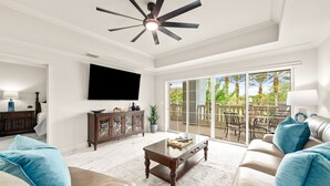 Ein geräumiges Wohnzimmer mit Deckenventilator, Flachbildfernseher, Couchtisch mit Glasplatte und einer großen Schiebeglastür zu einer Außenpatio-Terrasse.