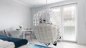 A modern room with a hanging chair, a dining area with a table and chairs, and a large window with blinds. - Elite Apartments Luna Studio (Gdansk)