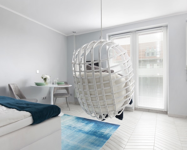 A modern room with a hanging chair, a dining area with a table and chairs, and a large window with blinds.