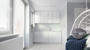 A modern kitchen with white cabinets, a herringbone floor pattern, and a hanging chair with cushions. - Elite Apartments Luna Studio (Gdansk)