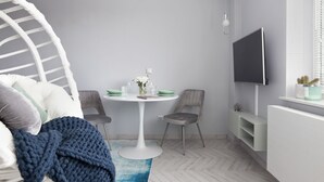 A modern room with a hanging chair, a dining table with chairs, a flat-screen TV, and a radiator. - Elite Apartments Luna Studio (Gdansk)
