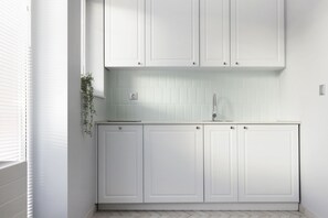 A modern kitchen with white cabinetry, a herringbone-patterned backsplash, and a window with blinds.