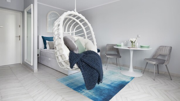 A modern room with a hanging chair, a dining table with chairs, and a bed with pillows. - Elite Apartments Luna Studio (Gdansk)