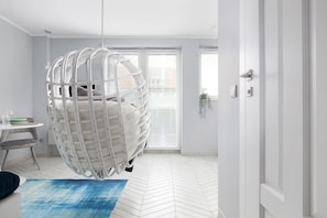 A modern room with a hanging chair, a small table with a green tray, and a blue rug. - Elite Apartments Luna Studio (Gdansk)