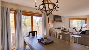 A spacious dining area with a wooden table, a chandelier, and a view of the outdoors through large windows. - Ski-in condo located 1 block from Main St w/ hot tubs, Covered parking, Fantasti (Breckenridge)