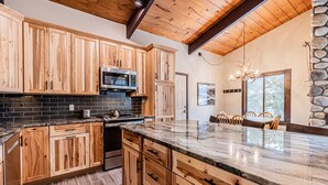 A kitchen with wooden cabinets, a granite countertop, and a stone wall. - Fireplace, Private Balcony, River/Forest Views! (Breckenridge)