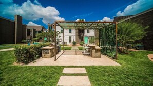 Ein Garten mit überdachter Terrasse, Grill und Sitzgruppe.