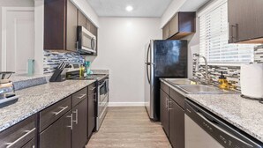 Eine moderne Küche mit dunklen Holzschränken, Granit Arbeitsplatten, einem Edelstahlkühlschrank und einer Mikrowelle.