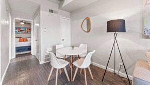 Una sala de estar moderna con una mesa redonda blanca, sillas blancas, una lámpara de pie y un espejo grande en la pared.
