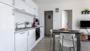 A modern kitchen with white cabinetry, a dining area with a table and chairs, and a television on a stand.
