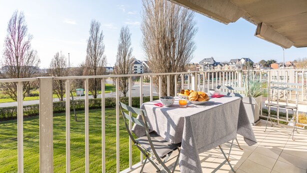 A balcony with a table set for breakfast, overlooking a residential area with houses and trees.