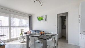 A modern dining area with a table set for four, white chairs, and a contemporary art piece on the wall.