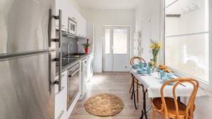Una cocina moderna con electrodomésticos de acero inoxidable, un comedor con una mesa lista para dos personas y vistas a través de un ventanal.